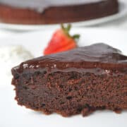 a slice of almost fudge gateau cake on a white plate with a strawberry in the background