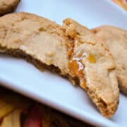 a browned butter cookie broken open on a plate to show the apple cider caramel filling inside