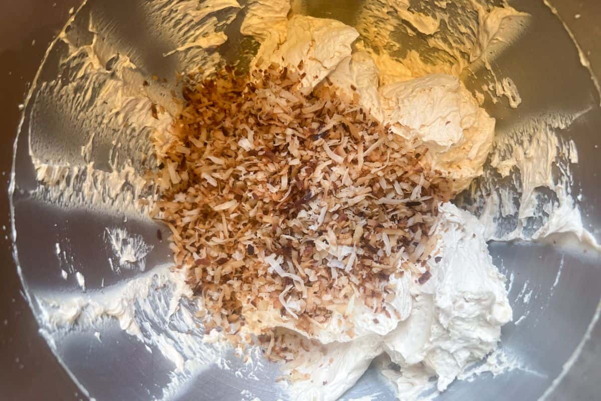 toasted coconut added to buttercream in a metal mixing bowl