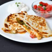 pico de gallo chicken quesadilla on a white plate with a bowl of pico de gally and a pile of sour cream