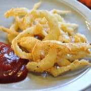 a plate of fried onion strings with ketchup on the side
