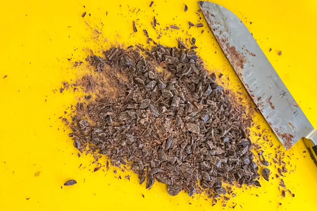 bittersweet chocolate chopped up on a cutting mat with a knife next to it