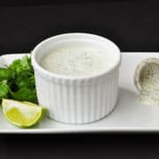 cilantro lime crema in a white ramekin on a white plate with limes and cilantro