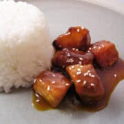 slow cooker orange chicken topped with sesame seeds on a plate next to a pile of white rice