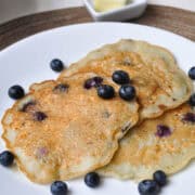 blueberry ricotta pancakes on a white plate with fresh blueberries scattered on the pancakes