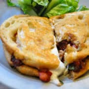 a Bruschetta Grilled Cheese Sandwich cut in half on a plate with lettuce in the background