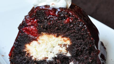 a slice of cherry chocolate cheesecake bundt cake on a white plate with whipped cream and cocoa powder on top
