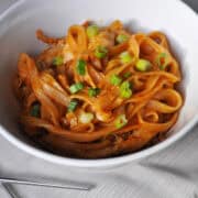 red curry rice noodles with chicken in a white bowl with metal chopsticks next to it