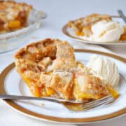 a slice of peach pie on a plate with a scoop of ice cream and a fork