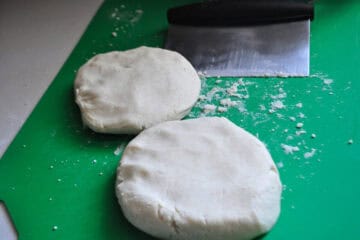 two discs of pie dough on a green cutting mat with a bench scraper