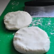two discs of pie dough on a green cutting mat with a bench scraper