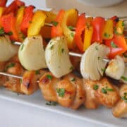 honey chicken kabobs on skewers and on a white plate