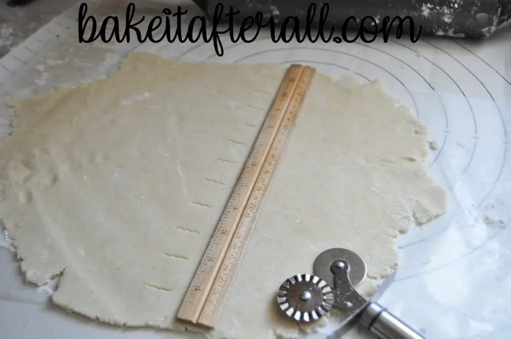 gluten free pie dough rolled thin on a pastry mat with a ruler on top and a double sided fluted cutter