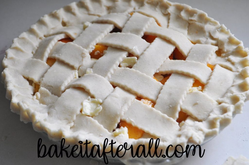 lattice top and fluted edges on fresh peach pie in glass pie plate before baking