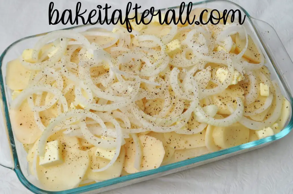 casserole dish with raw potatoes and slices of onions on top before baking