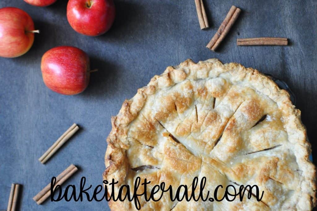 classic apple pie on a wood table with cinnamon sticks and apples