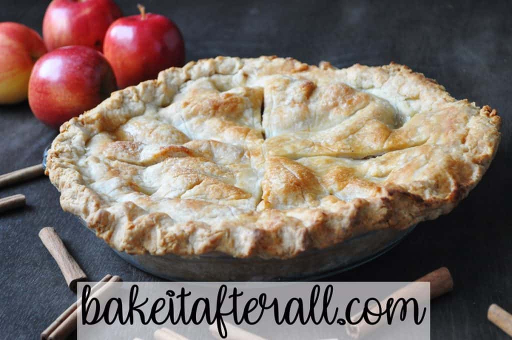 classic apple pie on a wood table with apples and cinnamon sticks