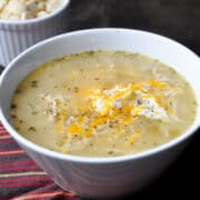 a white bowl with white chicken chili topped with sour cream and shredded cheese