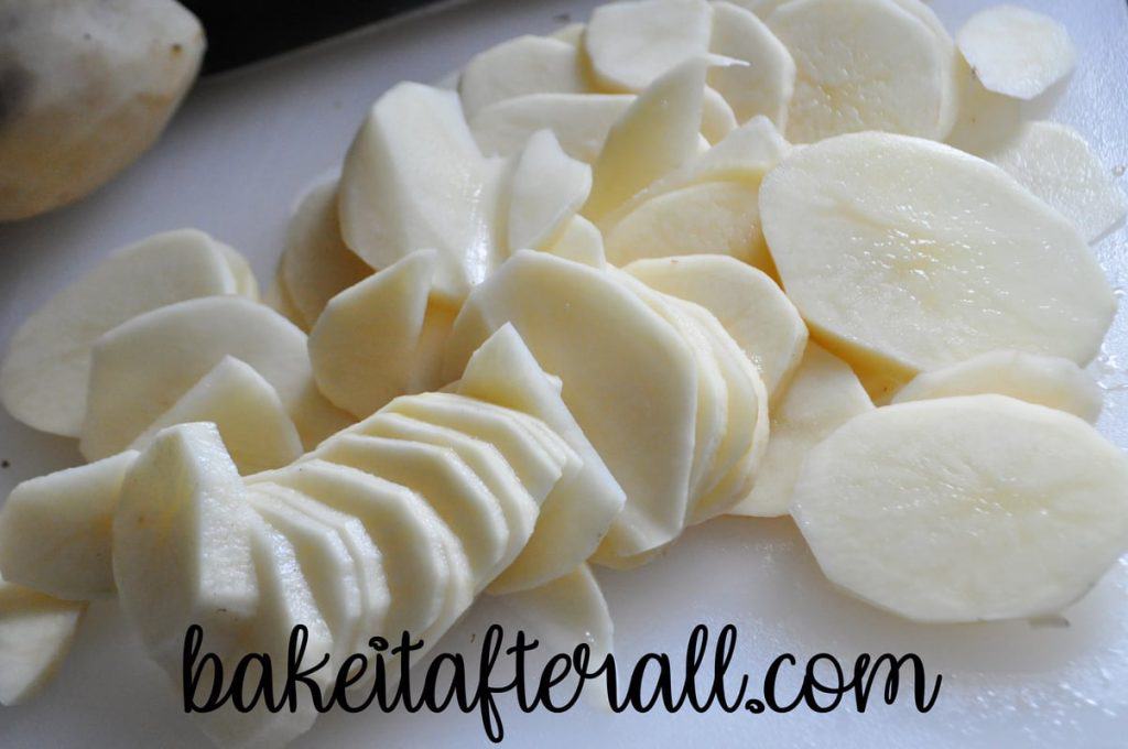 peeled and thinly sliced potatoes on a cutting board