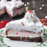 a slice of brownie peppermint ice cream cake on a holiday plate with lights in the background
