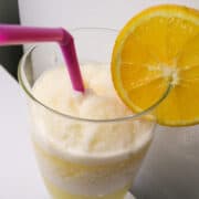 a glass of Orange Julius with an orange slice on the rim and a straw