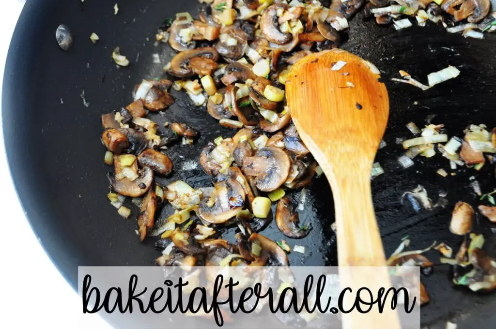 mushrooms and leeks in a skillet with a wooden spoon