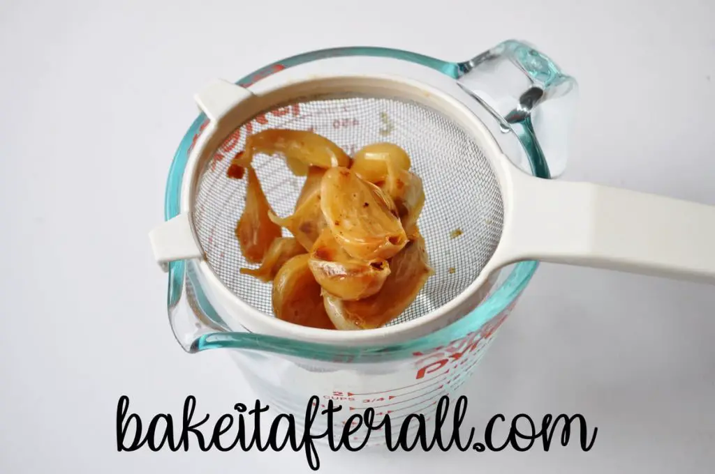 roasted garlic in a strainer set over a measuring cup