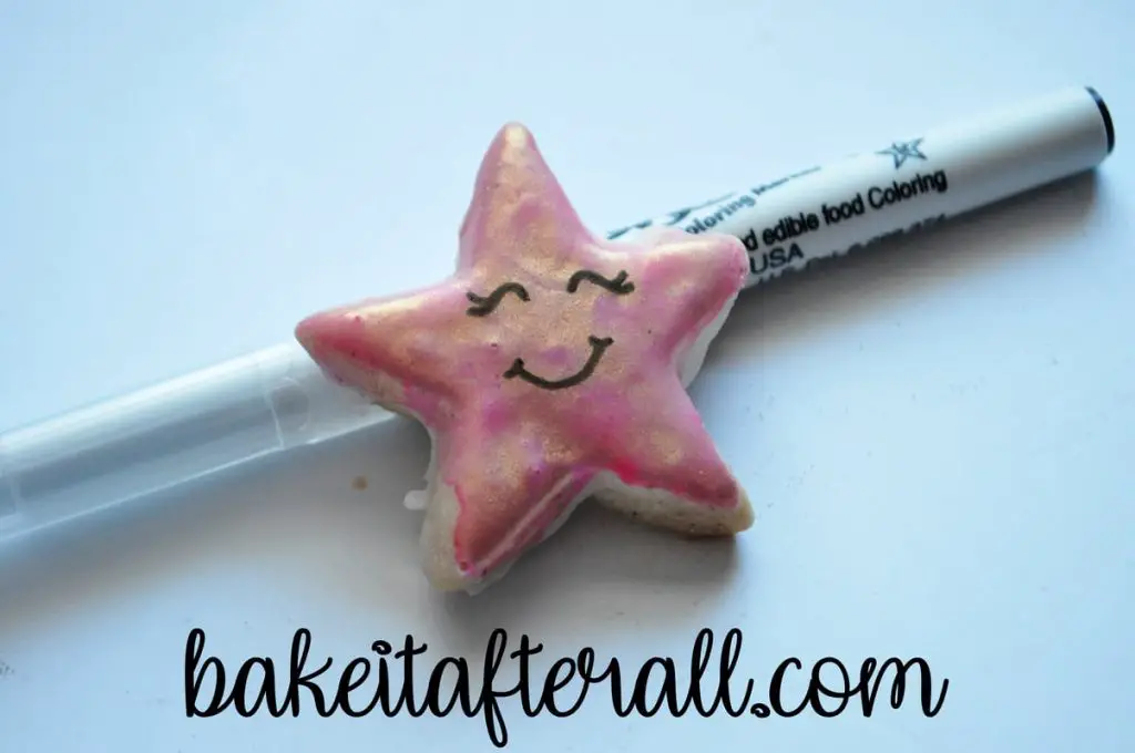 smiling painted watercolor cookie shaped like a star propped on a food coloring pen