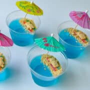 Beach Bear Jello Cups with blue jello and little teddy grahams laying on candy blankets underneath cocktail umbrellas