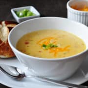 Wisconsin beer cheese soup in a white bowl with a pretzel roll next to it