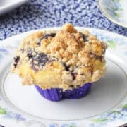 a blueberry muffin with a crumb topping on a flowered China plate