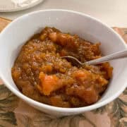 a white bowl of candied yams with a metal spoon in it