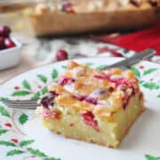 a square of Cranberry Christmas Cake on a holiday plate with fresh cranberries in the background
