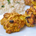 oven tandoori chicken on a white plate with basmati rice behind it