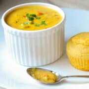 a bowl of broccoli cheddar soup in a white ramekin on a white plate with corn muffin next to it