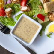 honey mustard dressing in a square white dish on a plate next to a salad