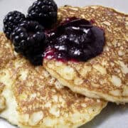 lemon ricotta pancakes on a plate with the syrup on top and fresh blackberries