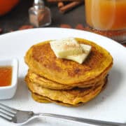 a stack of pumpkin pancakes on a white plate with squares of butter on top