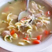 homemade turkey soup in a bowl with a metal spoon lifting out of the soup