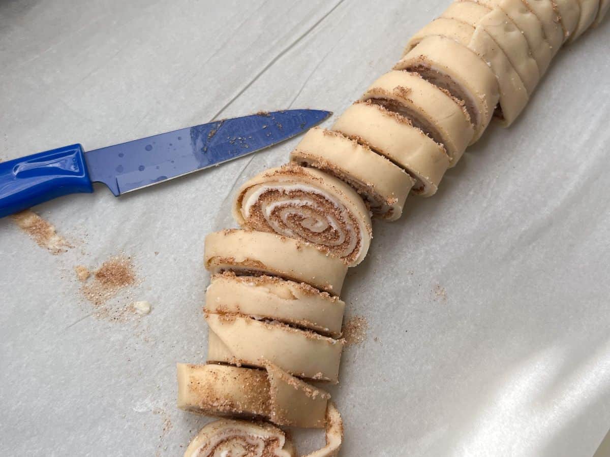 rolled up cinnamon cookies cut on a piece of parchment paper with a blue paring knife next to it