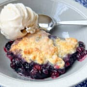 blueberry cobbler in a bowl with a scoop of vanilla ice cream and a spoon