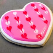 a Valentine Sugar Cookie with Royal Icing on a plate with little red and white hearts on a pink background