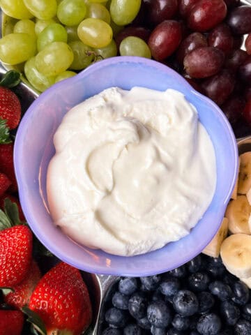 a purple bowl filled with fruit dip surrounded by fruit