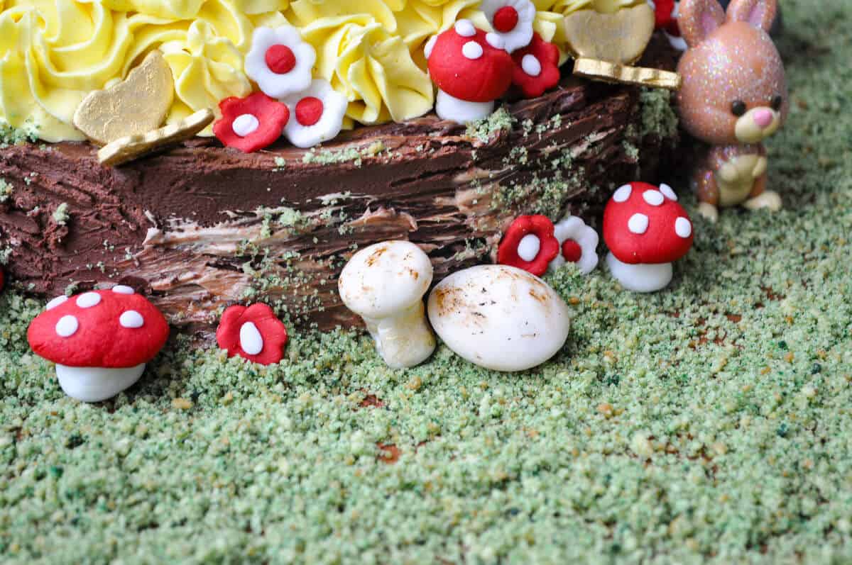 the base of a Snow White Doll Cake showing fondant mushrooms and flower and edible cookie moss on the cake board to mimic a forest floor