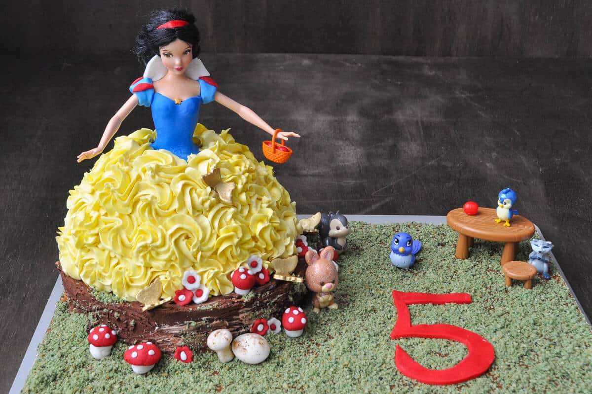 a Snow White Doll Cake on a cake board with edible cookie moss and a 5 made of red fondant