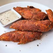 Blackened chicken tenders on a white plate with a dish of ranch dressing