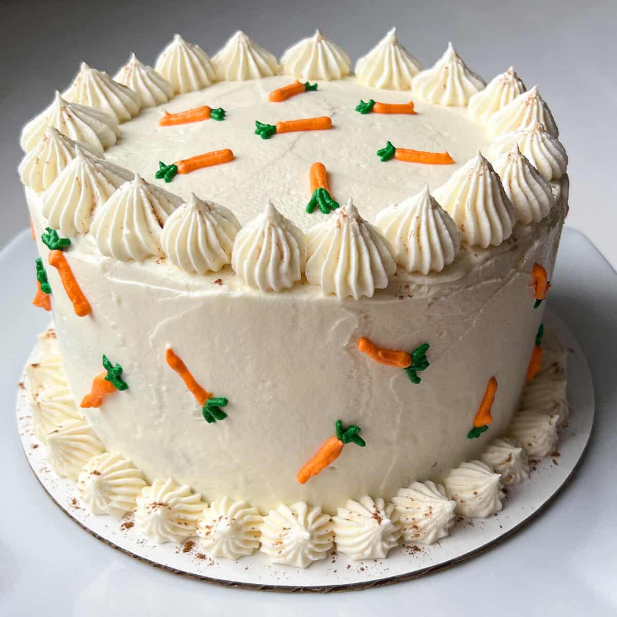 Nut Free Carrot Cake on a cardboard cake circle with small orange carrots piped on it