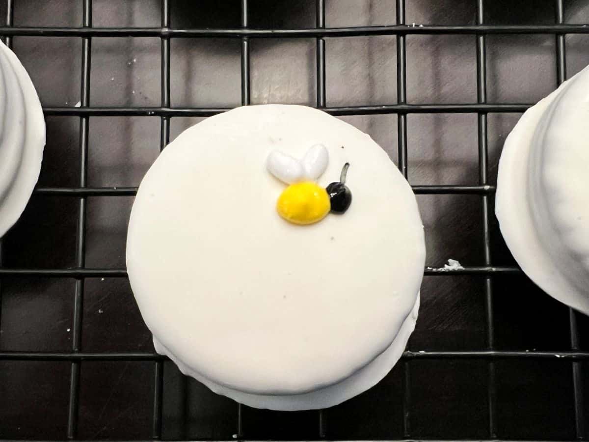 a bee made of royal icing on a white fudge covered Oreo
