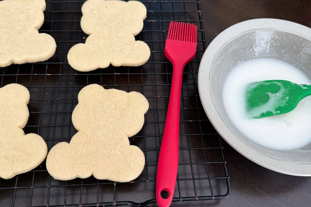sugar cookies in shape of polar bears next to a bowl of icing and a small silicone basting brush