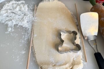 sugar cookie dough rolled between wooden dowel rods and cut with a teddy bear cookie cutter
